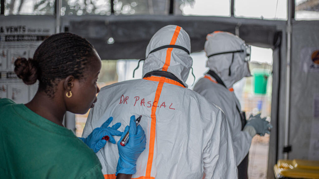 Agent d'hygiène africain notant le nom d'un médecin sur sa combinaison de protection avant d'entrer dans un centre de traitement Ebola à Bunia, en Ituri, dans l'est de la République démocratique du Congo